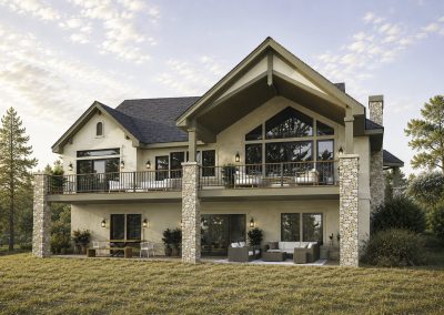 Two-story home exterior showing stacked stone chimneys, extensive glazing, covered upper deck with metal railings, and lower patio seating area