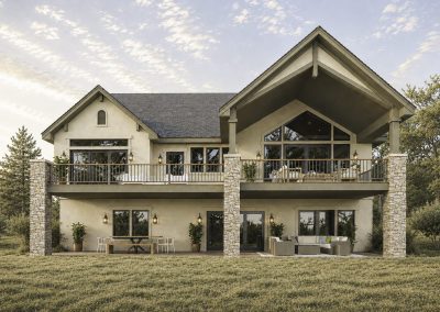 Two-story contemporary home with cream-colored exterior, prominent stacked stone columns, expansive covered deck with metal railings, large multi-pane windows, and gabled roofline against sky.